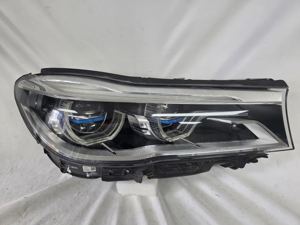 Used genuine BMW Laser headlight for 7 Series models G11 and G12. This right-side OEM headlamp, part number 7465606, features advanced laser lighting technology for superior visibility and performance. The image shows the original BMW right laser headlight in used condition, highlighting the detailed lens design, housing structure, and connector ports — ideal for high-end replacement or repair on compatible 7 Series vehicles.