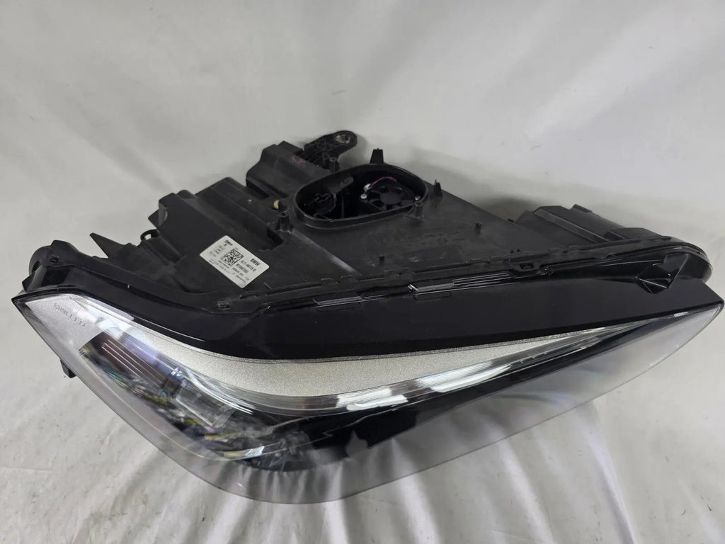Used genuine BMW Adaptive LED headlight for X1 F48 LCI (facelift) model. This right-side OEM headlamp, part number 5A01178, is equipped with adaptive lighting technology for improved night visibility and cornering performance. The image displays the original right Adaptive LED headlight in used condition, showing the clear lens, mounting brackets, and electrical connectors — an ideal OEM replacement for BMW X1 F48 LCI vehicles.