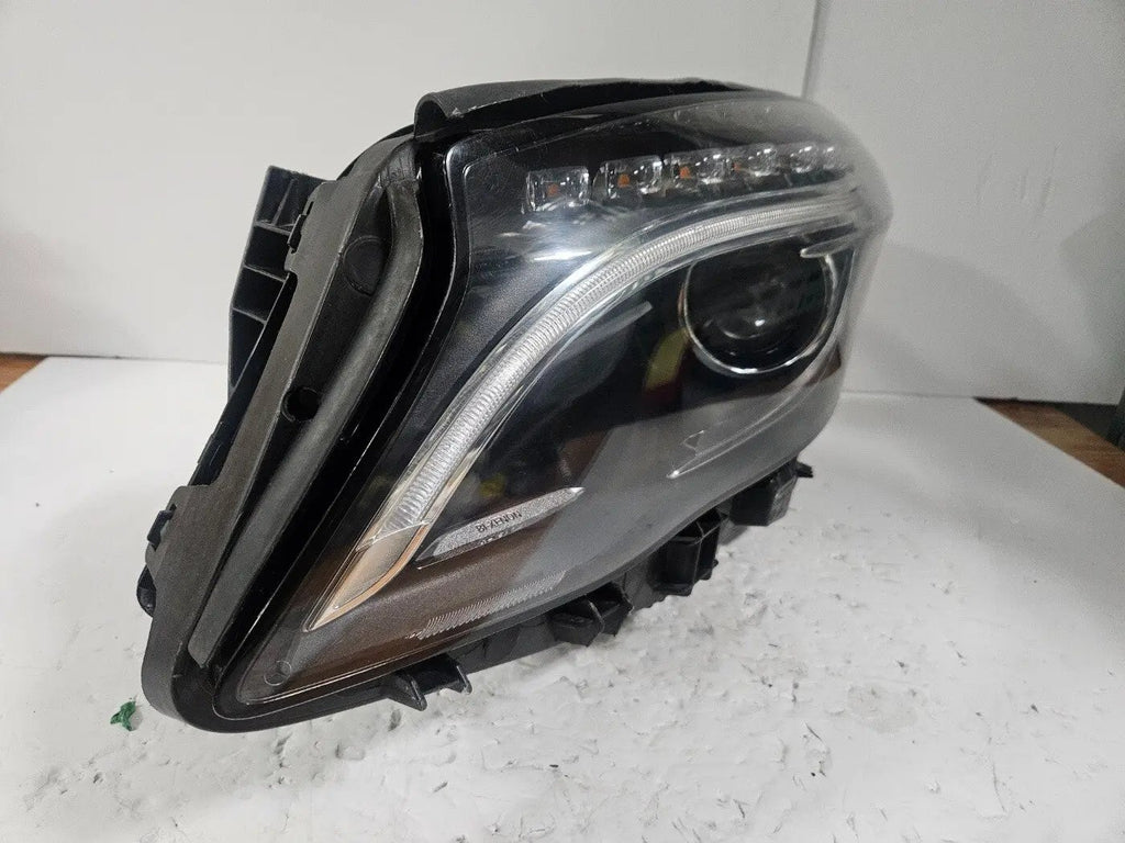 Genuine used Mercedes-Benz Bi-Xenon headlight for GLA-Class model X156. This left-side (LH) OEM headlamp, part number A1569061700, features Bi-Xenon lighting technology for enhanced night visibility and a focused beam pattern. The image shows the original left headlight in used condition, highlighting the lens clarity, projector unit, mounting brackets, and electrical connector — ideal for replacing a damaged headlamp on compatible Mercedes-Benz GLA X156 vehicles.