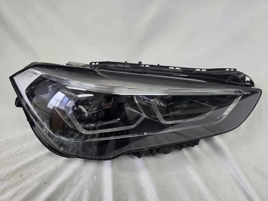 Used genuine BMW Adaptive LED headlight for X1 F48 LCI (facelift) model. This right-side OEM headlamp, part number 5A01178, is equipped with adaptive lighting technology for improved night visibility and cornering performance. The image displays the original right Adaptive LED headlight in used condition, showing the clear lens, mounting brackets, and electrical connectors — an ideal OEM replacement for BMW X1 F48 LCI vehicles.