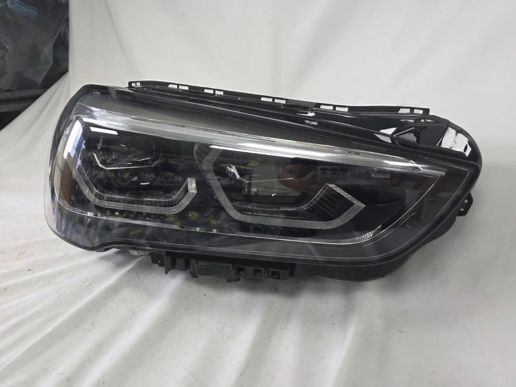 Used genuine BMW Adaptive LED headlight for X1 F48 LCI (facelift) model. This right-side OEM headlamp, part number 5A01178, is equipped with adaptive lighting technology for improved night visibility and cornering performance. The image displays the original right Adaptive LED headlight in used condition, showing the clear lens, mounting brackets, and electrical connectors — an ideal OEM replacement for BMW X1 F48 LCI vehicles.