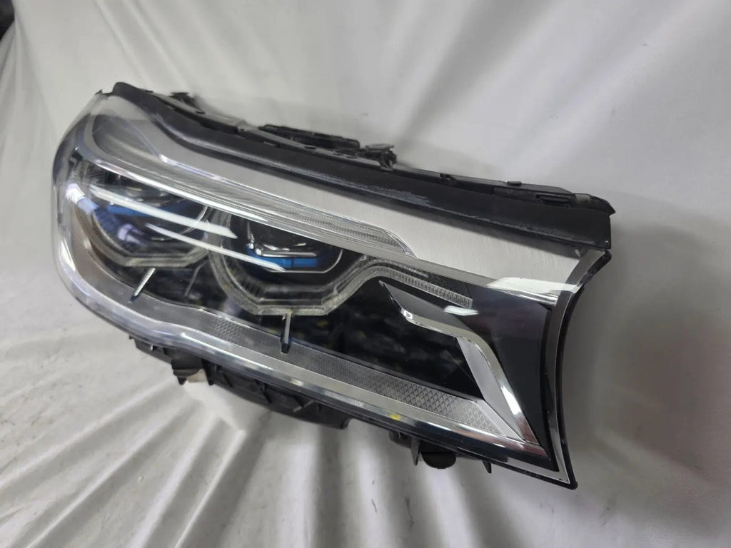Used genuine BMW Laser headlight for 7 Series models G11 and G12. This right-side OEM headlamp, part number 7465606, features advanced laser lighting technology for superior visibility and performance. The image shows the original BMW right laser headlight in used condition, highlighting the detailed lens design, housing structure, and connector ports — ideal for high-end replacement or repair on compatible 7 Series vehicles.