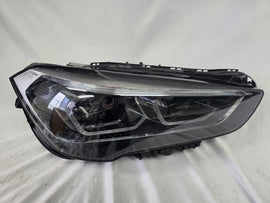 Used genuine BMW Adaptive LED headlight for X1 F48 LCI (facelift) model. This right-side OEM headlamp, part number 5A01178, is equipped with adaptive lighting technology for improved night visibility and cornering performance. The image displays the original right Adaptive LED headlight in used condition, showing the clear lens, mounting brackets, and electrical connectors — an ideal OEM replacement for BMW X1 F48 LCI vehicles.
